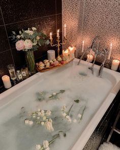 a bath tub filled with lots of water next to candles and flowers on the floor