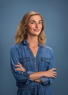 a woman with her arms crossed and looking at the camera while wearing a denim jumpsuit