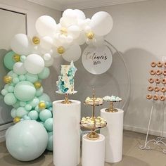 balloons and desserts are on display in a room decorated with white, gold and mint green colors