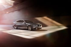 a silver car driving down a street next to a tall brick wall with light coming through it