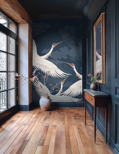 two white birds are flying in the air over a wood floored room with large windows