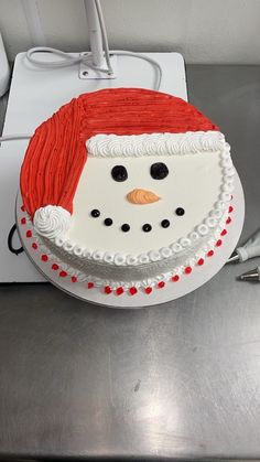 a cake decorated like a snowman sitting on top of a metal counter next to a white box