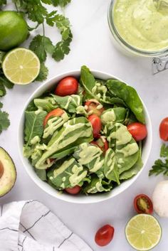 a white bowl filled with lettuce and tomatoes next to sliced avocado