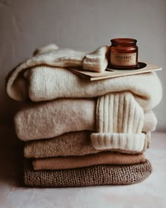 a stack of folded sweaters with a jar of cream on top and a book