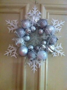 a snowflake wreath with ornaments hanging from the front door, decorated with silver and white baubles