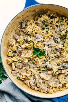 a pot filled with pasta and mushrooms on top of a blue cloth next to parsley