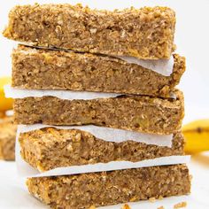 four granola bars stacked on top of each other with bananas in the back ground