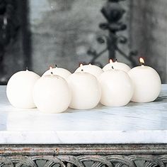 five white candles are lined up on a marble table in front of a fire place