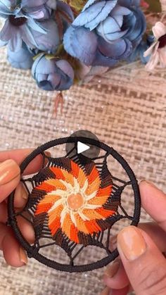 two hands are holding an orange and black flower brooch on a piece of fabric