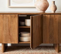 a wooden cabinet with plates and vases on it's sideboard in a living room