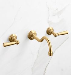 two golden handles on a marble wall mounted faucet in an elegant bathroom setting