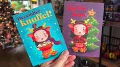 two children's books are held up in front of a christmas tree with lights