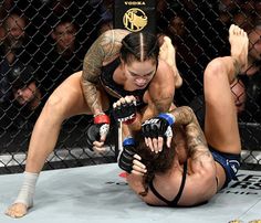 two women wrestling in a caged area with one holding the other's leg