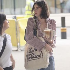 a woman is walking down the street with a coffee cup in her hand and two other women are talking to each other