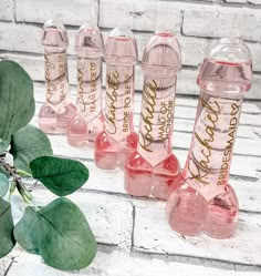 five pink glass bottles with gold lettering on them sitting next to a leafy branch