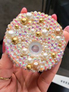 a hand holding a button made out of pearls and other beads with gold balls on it