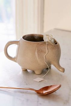 an elephant shaped coffee cup and spoon on a white counter top with a window in the background