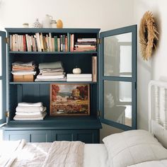 a book shelf with books and blankets on top of it in a bedroom next to a bed