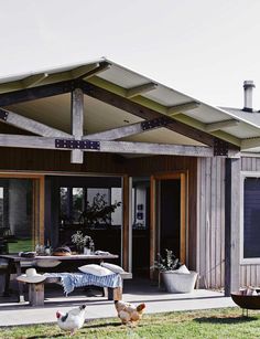 two chickens are standing in front of a house with an open porch and covered patio