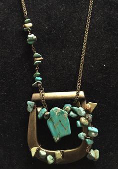 a necklace with turquoise stones and gold chains on a black surface, including an arrow