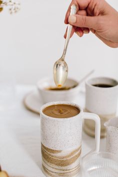 a person is spooning some liquid out of a cup with another mug in the background