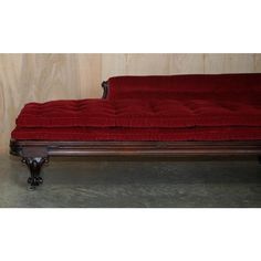 a red couch sitting on top of a cement floor next to a wooden paneled wall