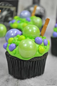 cupcakes decorated with green and purple icing on top of black paper cups