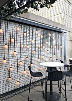 an outdoor dining area with tables and chairs next to a brick wall filled with lit candles