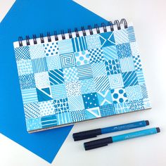 a notebook and two pens sitting on top of a blue table cloth covered in patchwork