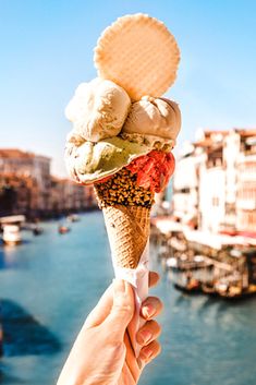 a person holding up an ice cream cone in front of a body of water with boats on it