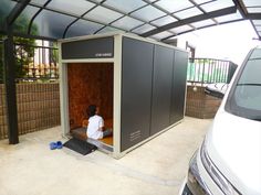 a man sitting inside of a small building next to a white car