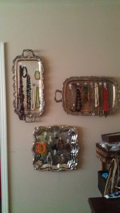 three silver trays are hanging on the wall next to each other, with beads and bracelets in them