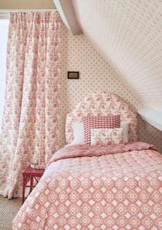 a bed sitting under a window in a bedroom next to a pink comforter and curtains