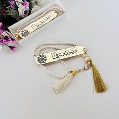 two tasseled key chains with arabic writing on them and flowers in the background