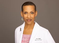 a woman in a white jacket and earrings posing for a photo on a gray background