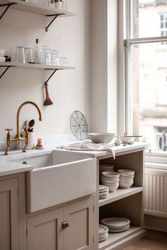 a kitchen with white walls and wooden flooring next to a window filled with dishes