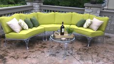 a yellow couch sitting on top of a patio next to a table with a bottle of wine