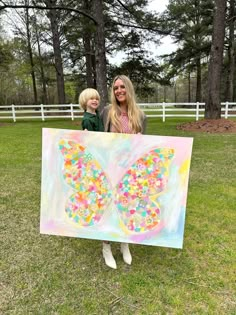 a woman and child holding up a butterfly painting