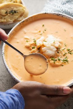 a person holding a spoon over a bowl of soup with cauliflower on top