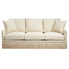 a white couch with fringe trim around the arms and back cushions, on a white background