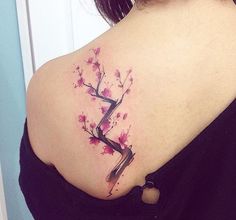 a woman's upper back tattoo with pink flowers on her left shoulder and the letter e painted in black ink