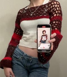 a woman holding a cell phone in her right hand and wearing a sweater on the other