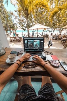 a person sitting in front of a laptop computer on top of a wooden table next to a beach