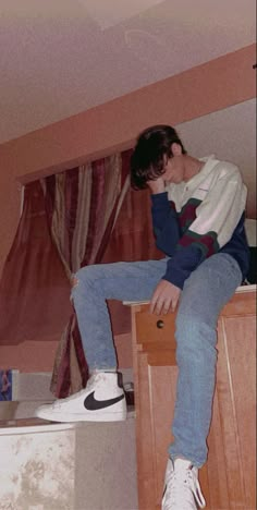 a young man sitting on top of a wooden dresser