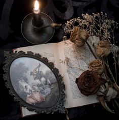 an open book sitting on top of a table next to a candle and some dried flowers