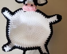 a crocheted black and white cow with a pink nose is hanging on the wall