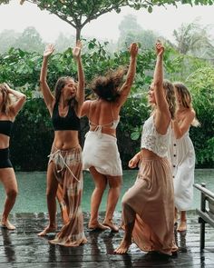 four women in bathing suits are dancing on a wooden dock with trees in the background