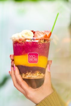 a woman holding up a smoothie with bananas and strawberries