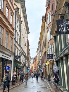 people are walking down the street in an old european town with tall buildings and shops