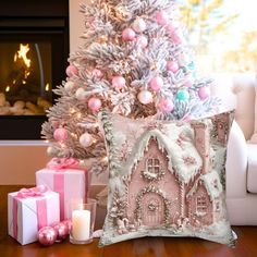 a white christmas tree with pink and silver ornaments next to a decorative pillow on a wooden table